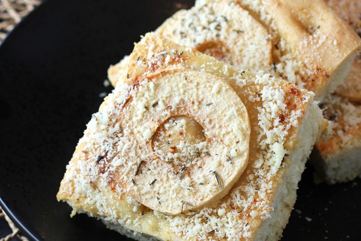 slices of focaccia stacked on a black plate. Each slice is topped with cheese, herbs, and a ring of pazazz apple slice.