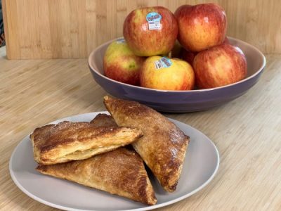 Freshly-baked Pazazz turnovers sitting on a plate in front of a bowl of Pazazz Apples.