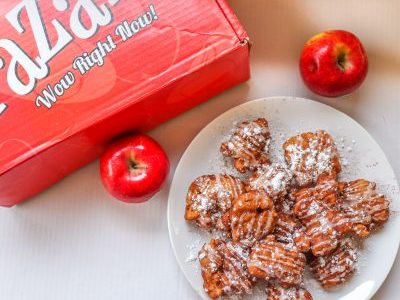 Plate of Pazazz apple fritters situated next to two shiny red Pazazz apples. A red Pazazz apple box that says "Wow Right Now" sits at the top left of the image.