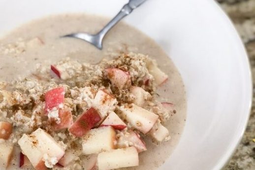 white bowl filled with oats and pazazz apples. Cinnamon is sprinkled on top. A metal spoon sits at the back of the bowl. Everything sits on top of the a beige granite countertop.