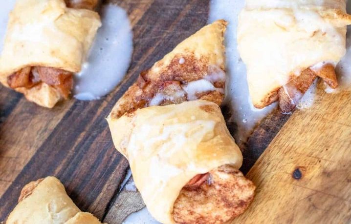 pastry wrapped around cinnamon coated apples and drizzled with a sugar glaze, all positioned on a wooden board