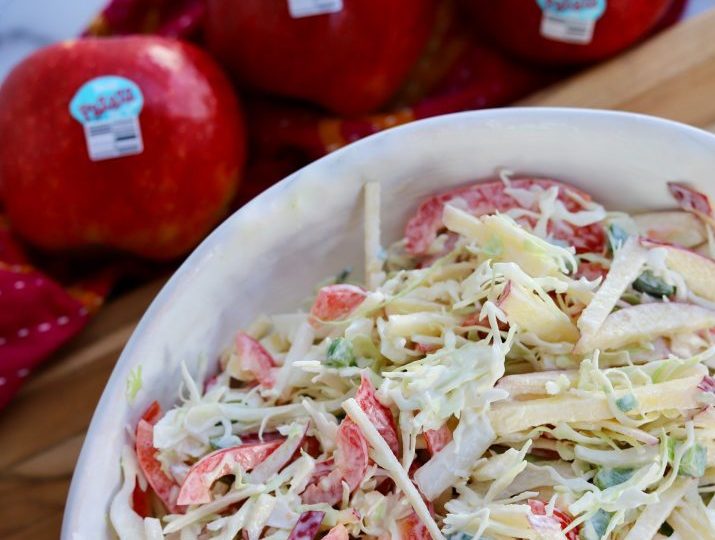 white ceramic bowl filled with apple coleslaw. It is positioned next to a red pazazz apple on a wooden counter.